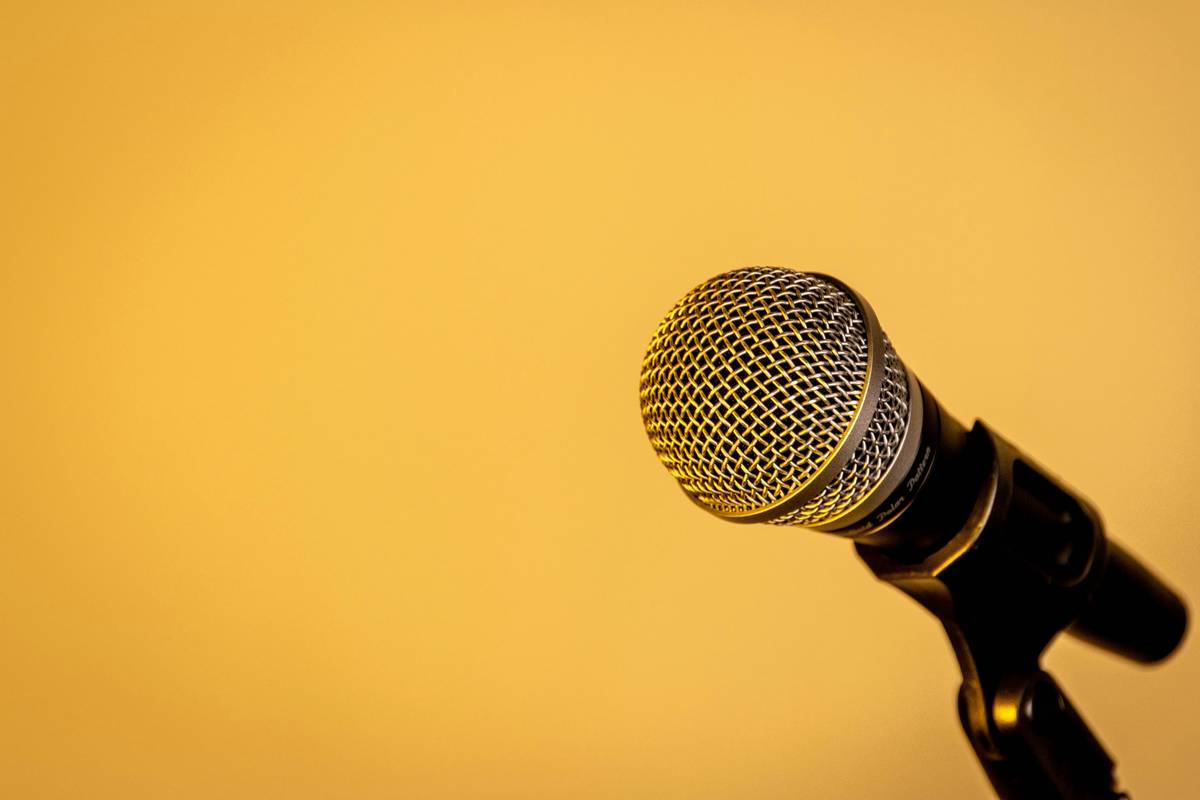 Close-up shot of a microphone with a metallic mesh head, set against a warm yellow background, with no other objects in the frame