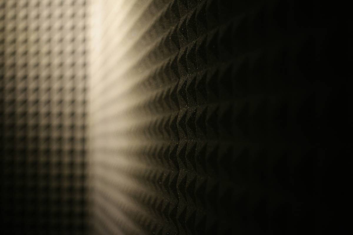 Diagram showing sound waves reflecting off untreated walls versus absorbed by foam tiles at primary reflection points